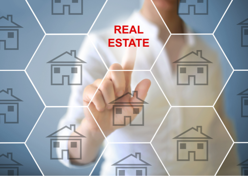 Finger pointing at “real estate” text written on a clear board